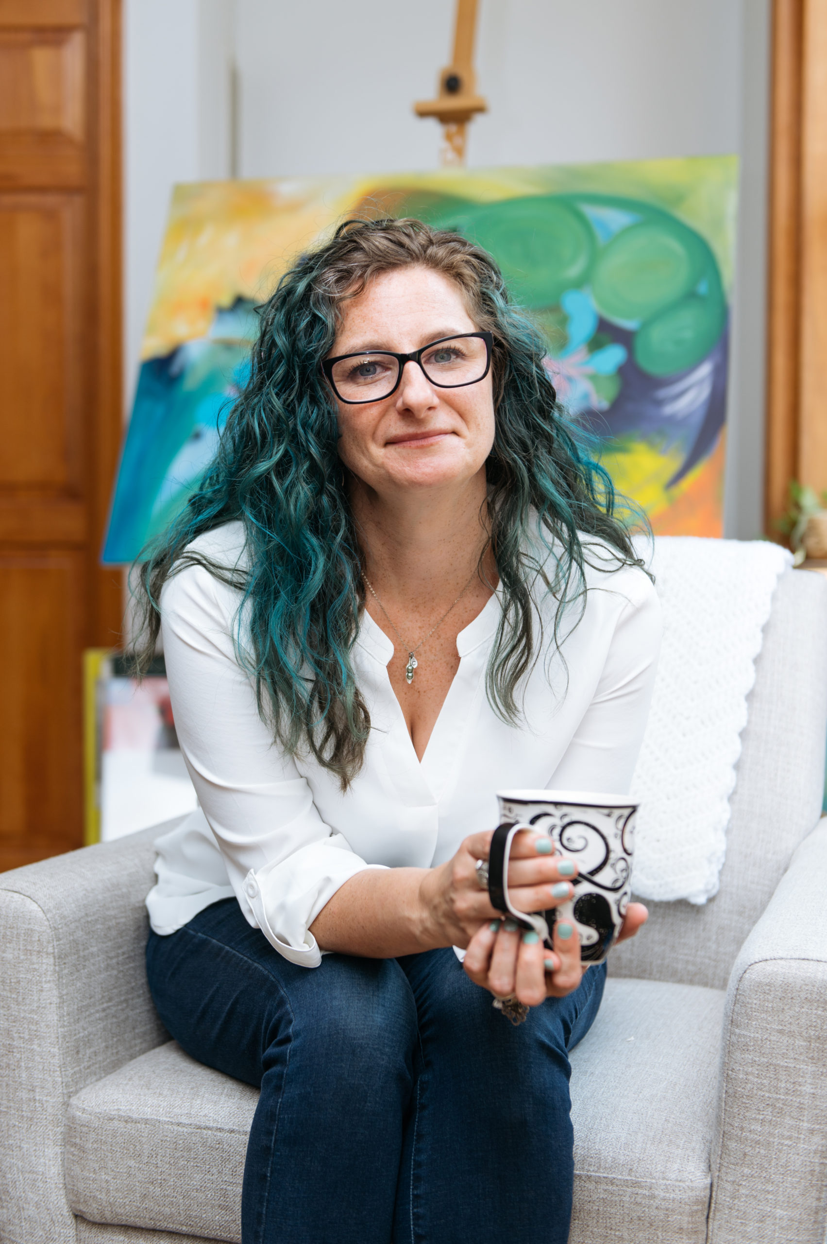 art therapist Sivan Perdue sitting with tea in front of painting